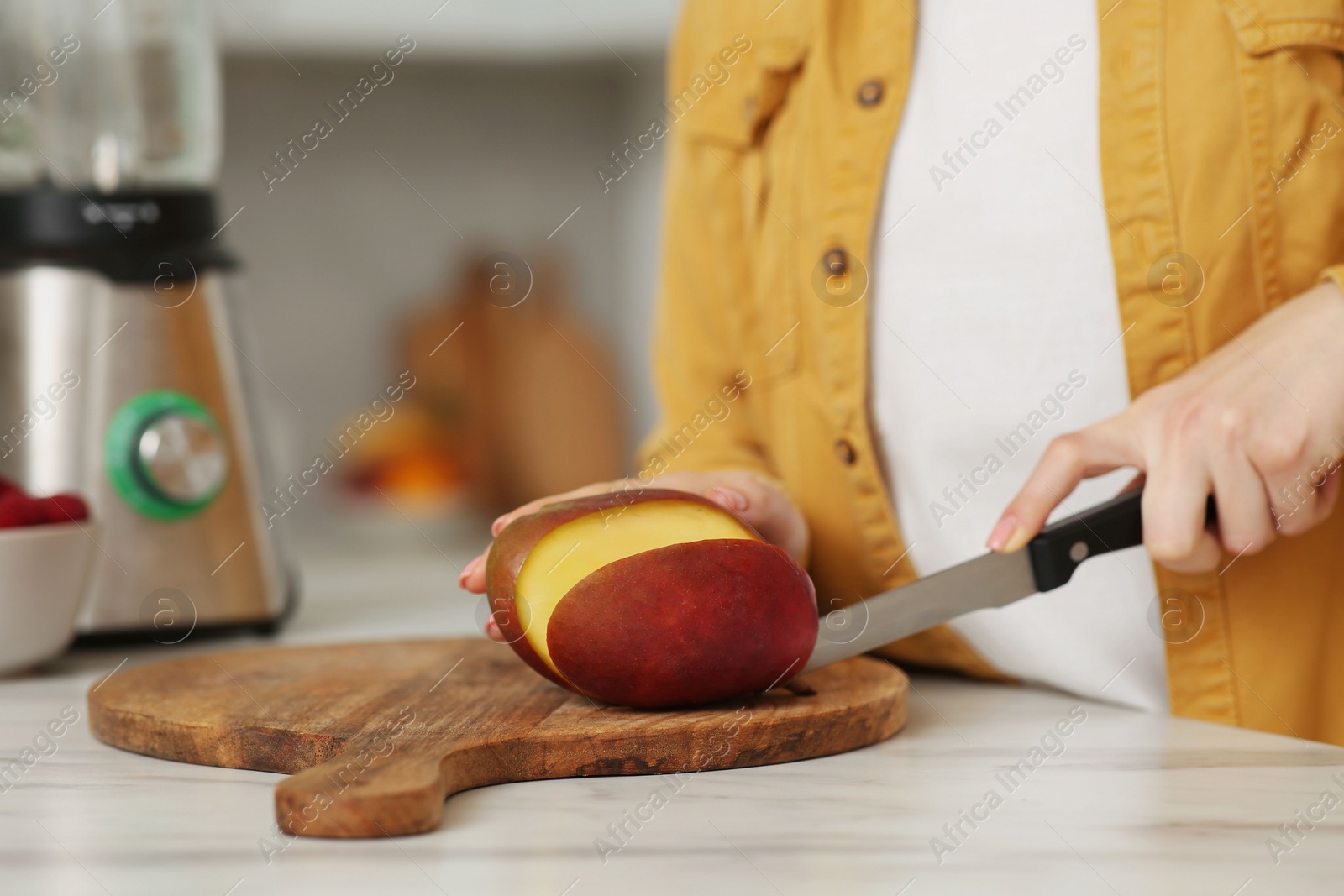 Photo of Woman preparing mango for tasty smoothie at white marble table in kitchen, closeup