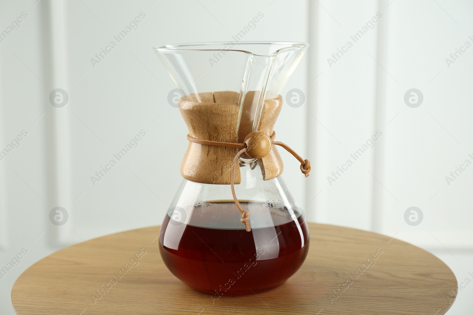 Photo of Glass chemex coffeemaker with coffee on wooden table against white wall