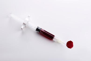 Plastic syringe with blood on white background, top view