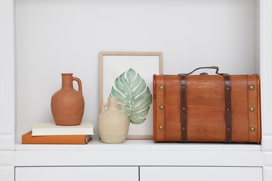 Brown suitcase, vases, books and picture on shelving unit indoors