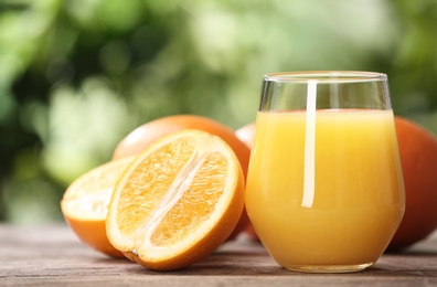 Glass of fresh juice and oranges on wooden table. Space for text