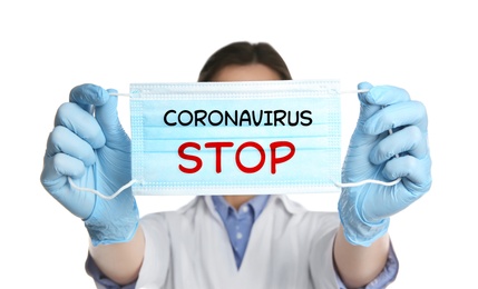 Doctor holding medical mask with text Coronavirus Stop on white background. Protective measures during pandemic