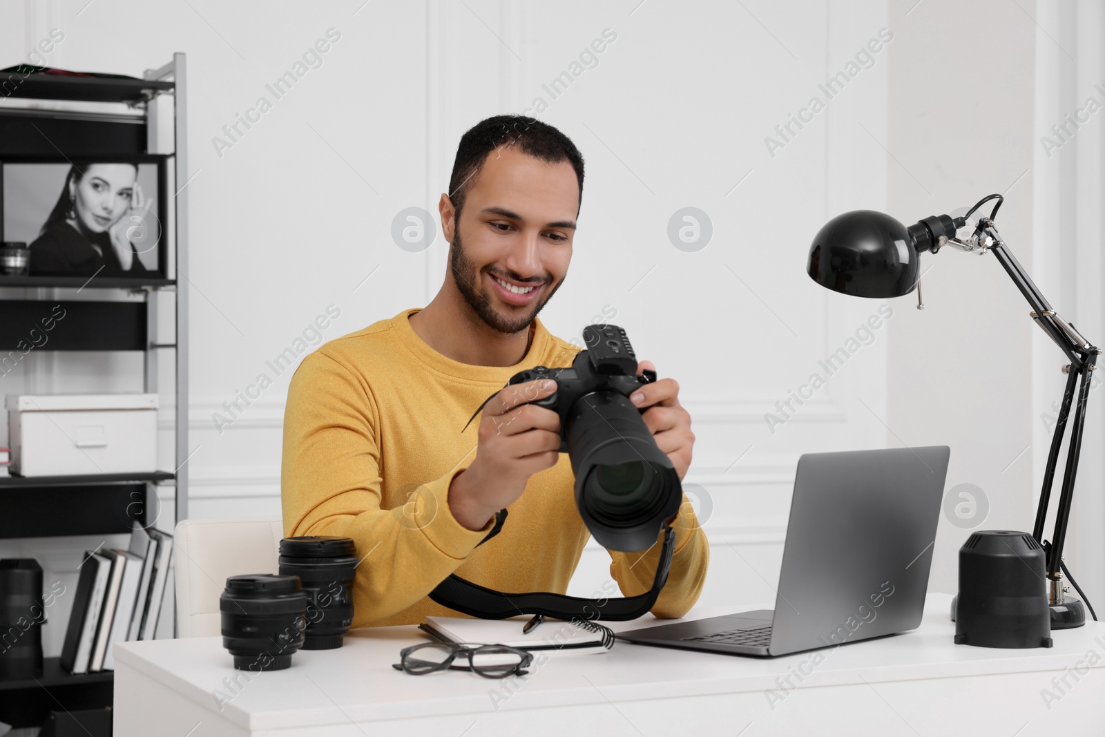 Photo of Young professional photographer with camera at table in modern photo studio