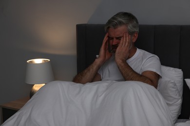 Photo of Mature man suffering from headache in bed at night