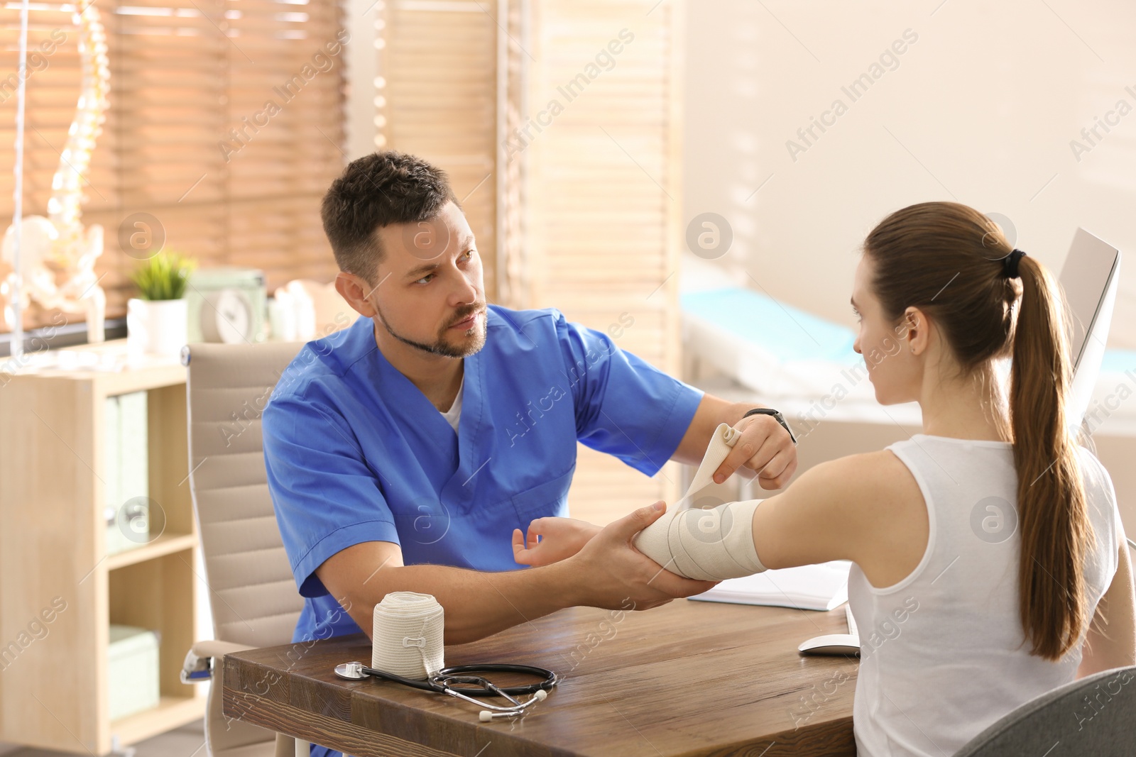 Photo of Male orthopedist applying bandage onto patient's elbow in clinic