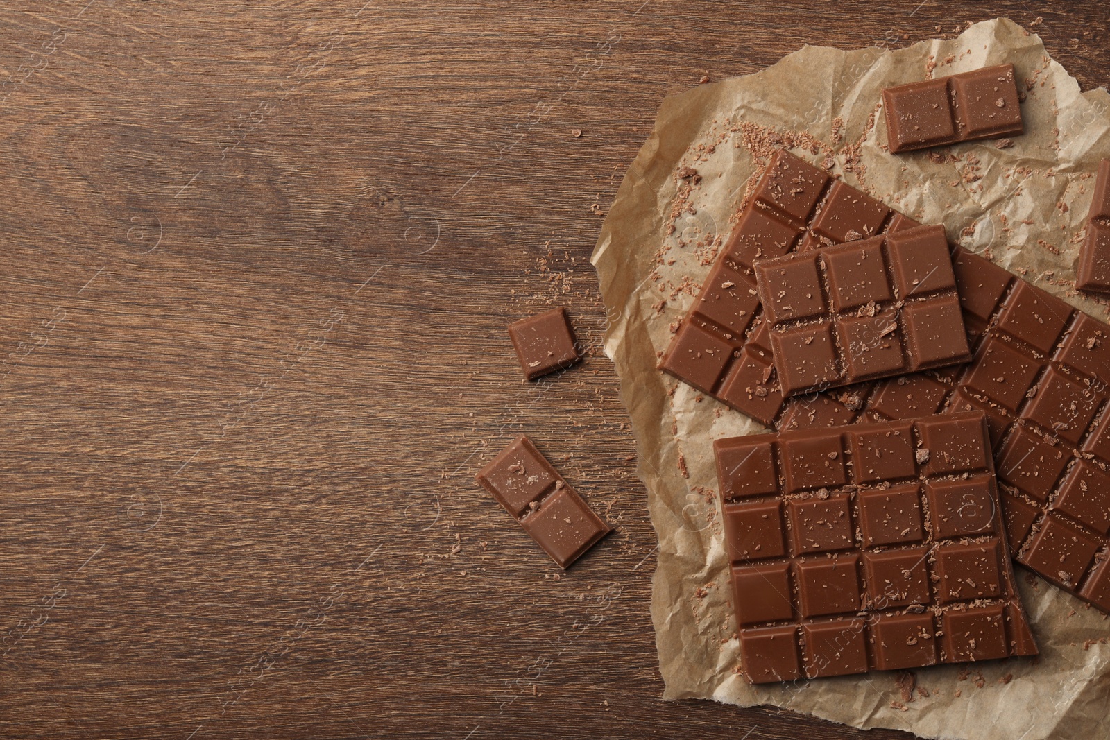 Photo of Pieces and crumbs of tasty chocolate bars on wooden table, flat lay. Space for text