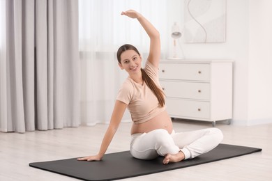 Photo of Pregnant woman doing exercises on yoga mat at home