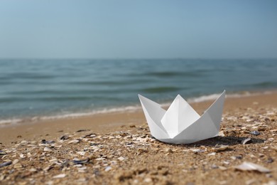 Photo of White paper boat on sandy beach near sea, space for text
