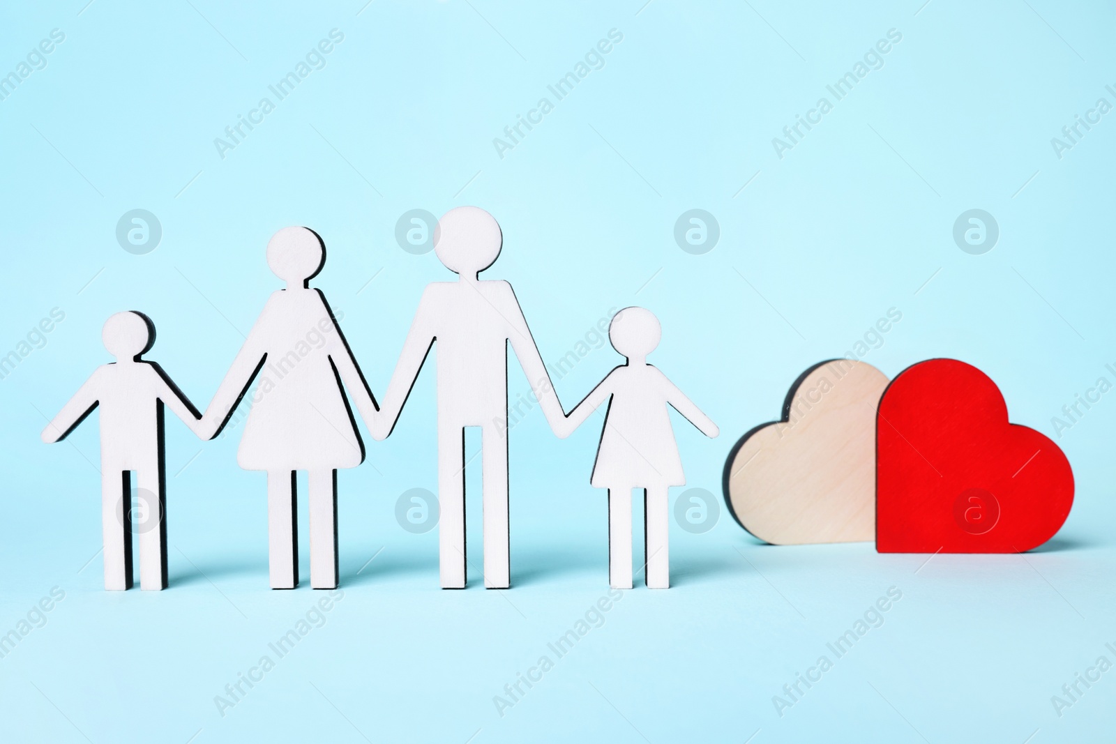 Photo of Figures of family stainding near heart on light blue background. Insurance concept