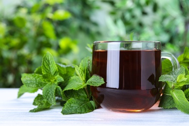 Photo of Fresh tea with mint leaves on white wooden table, closeup