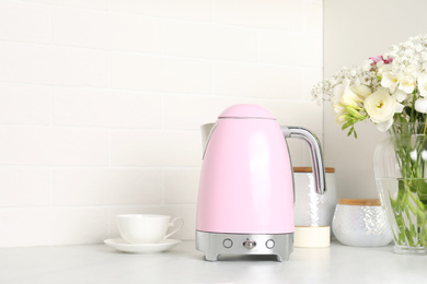 Modern electric kettle, cup and bouquet on counter in kitchen