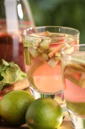 Photo of Glasses of tasty rhubarb cocktail and lime fruits on table outdoors, closeup