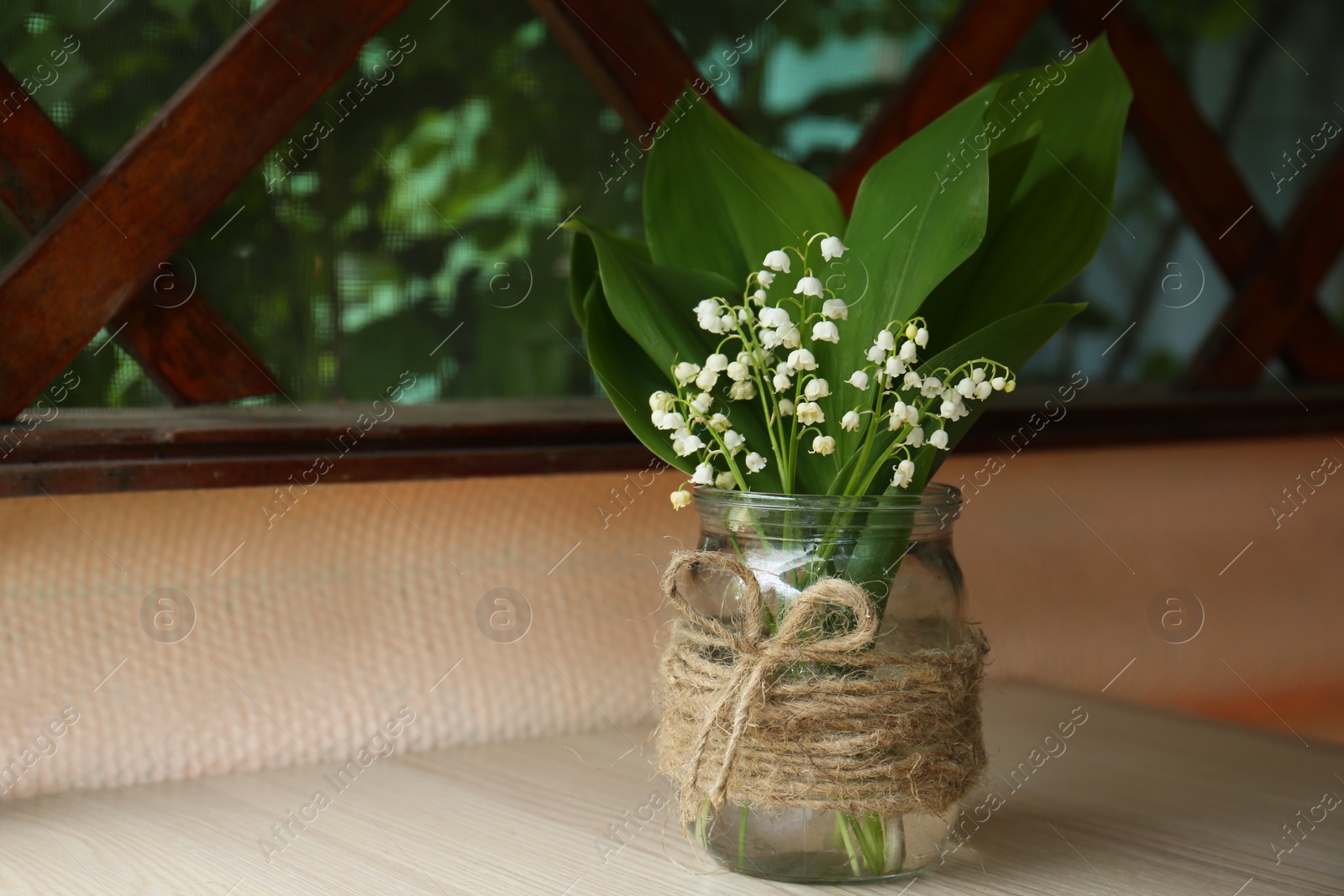 Photo of Beautiful lily of the valley flowers in glass vase on wooden table indoors, space for text