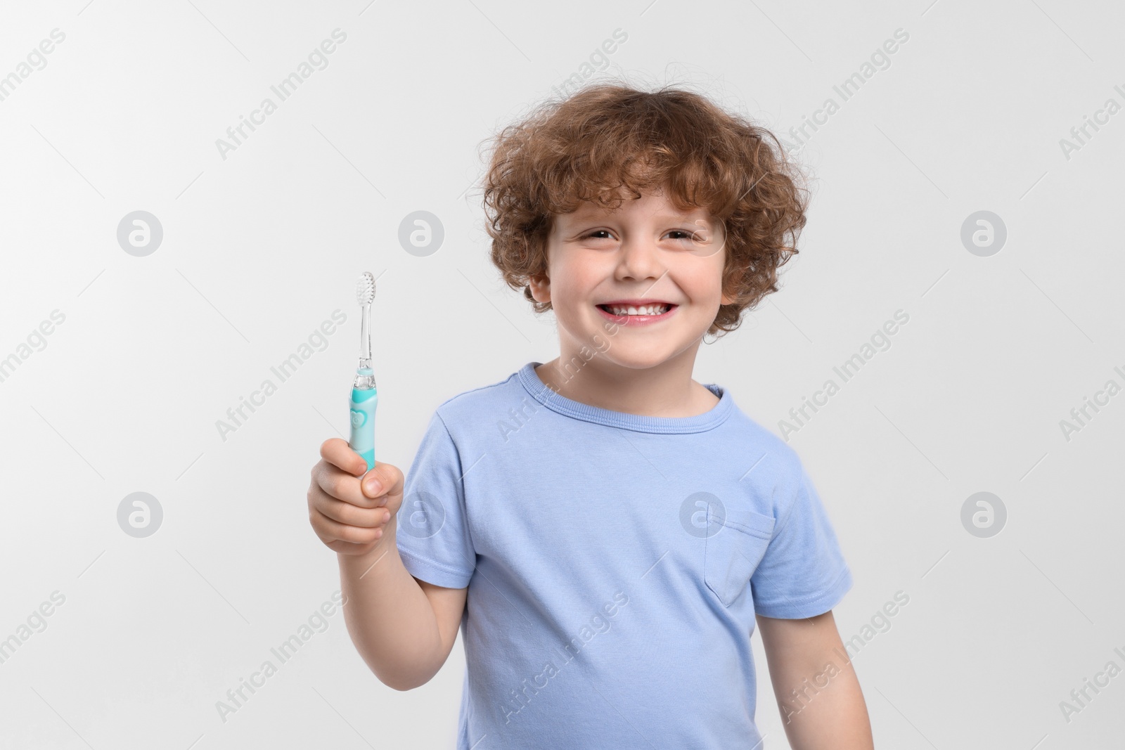 Photo of Cute little boy holding electric toothbrush on white background