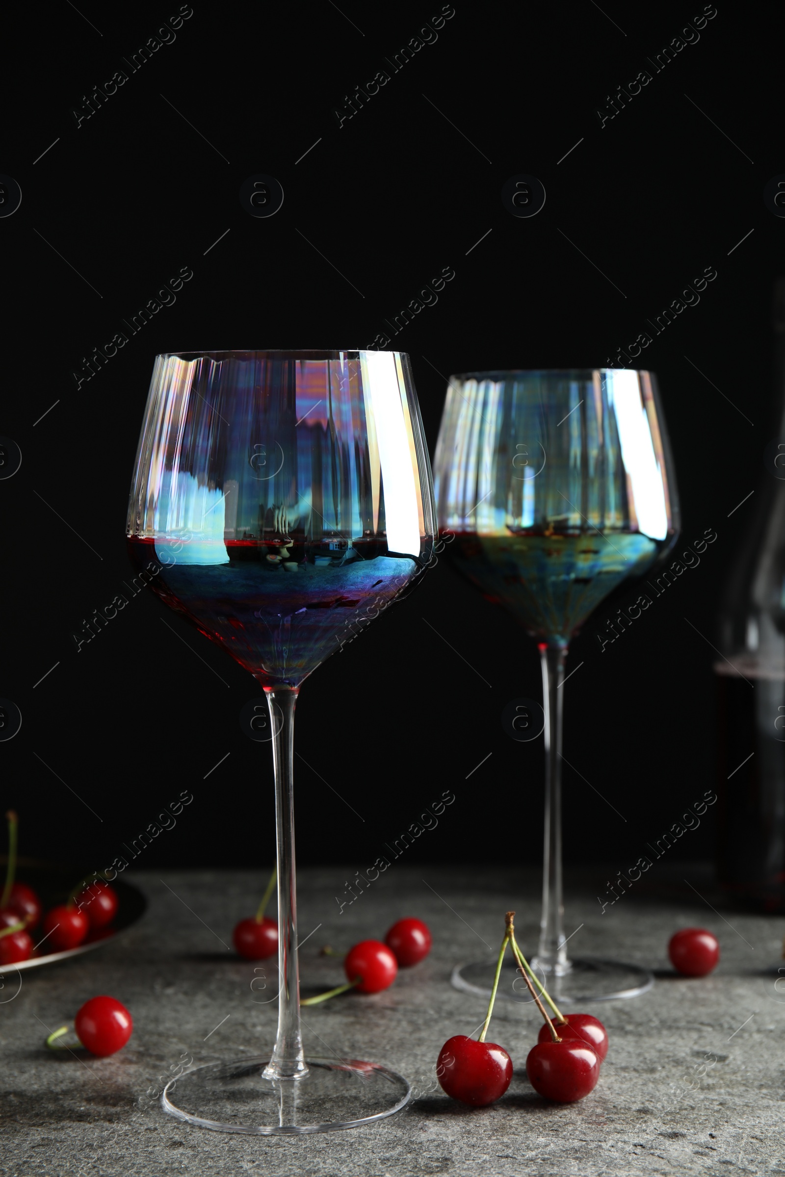 Photo of Delicious cherry wine with ripe juicy berries on grey table against black background