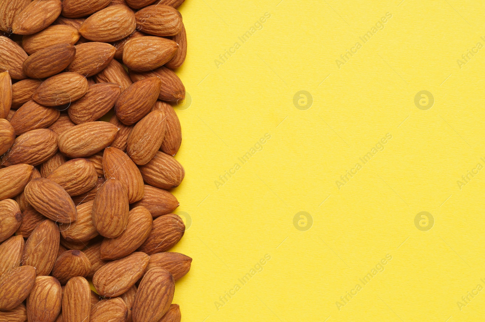 Photo of Delicious raw almonds on yellow background, flat lay. Space for text