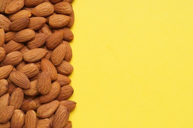 Photo of Delicious raw almonds on yellow background, flat lay. Space for text