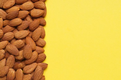 Delicious raw almonds on yellow background, flat lay. Space for text