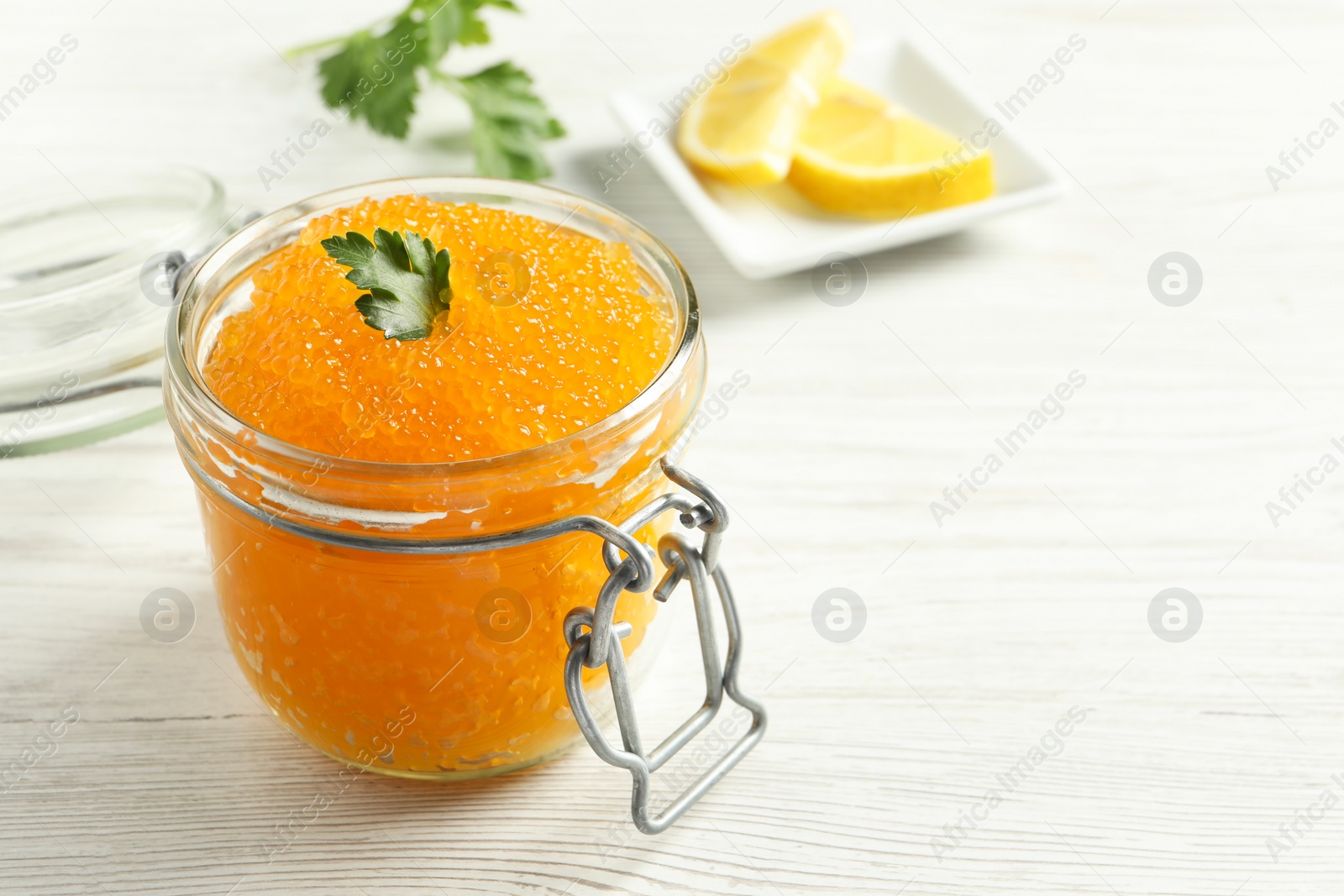 Photo of Fresh pike caviar in glass jar and parsley on light wooden table, closeup. Space for text