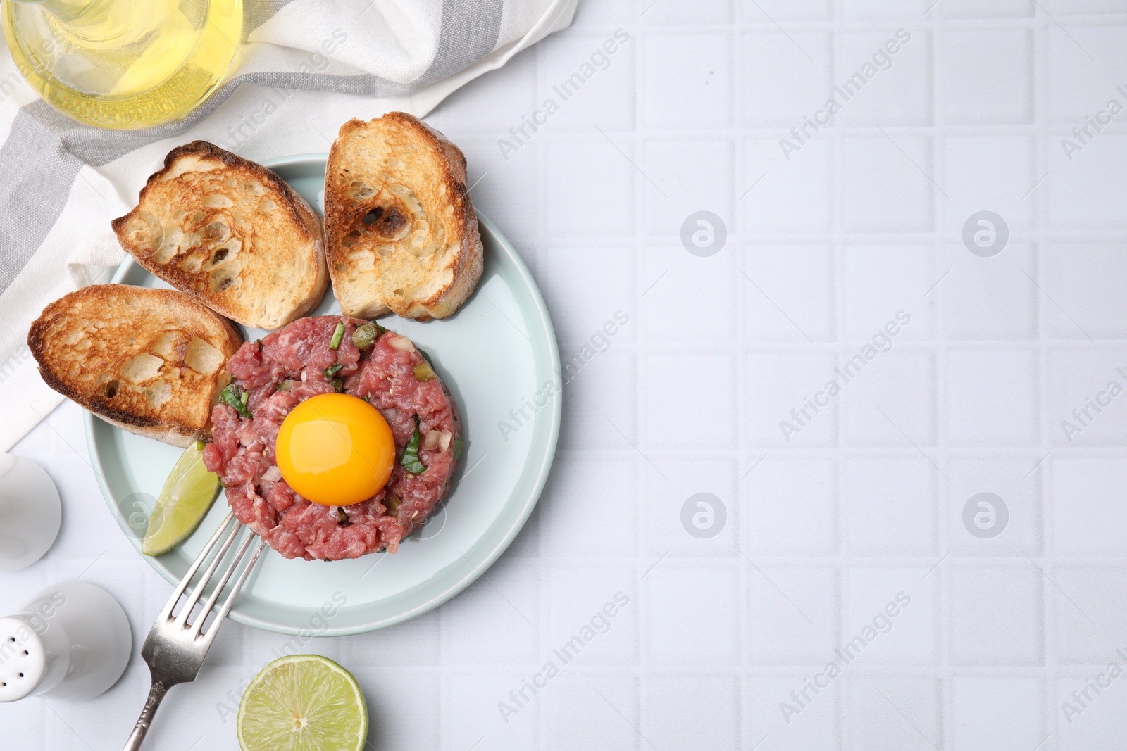 Photo of Tasty beef steak tartare served with yolk, toasted bread and lime on white tiled table, flat lay. Space for text