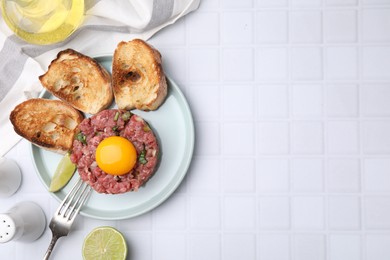 Tasty beef steak tartare served with yolk, toasted bread and lime on white tiled table, flat lay. Space for text