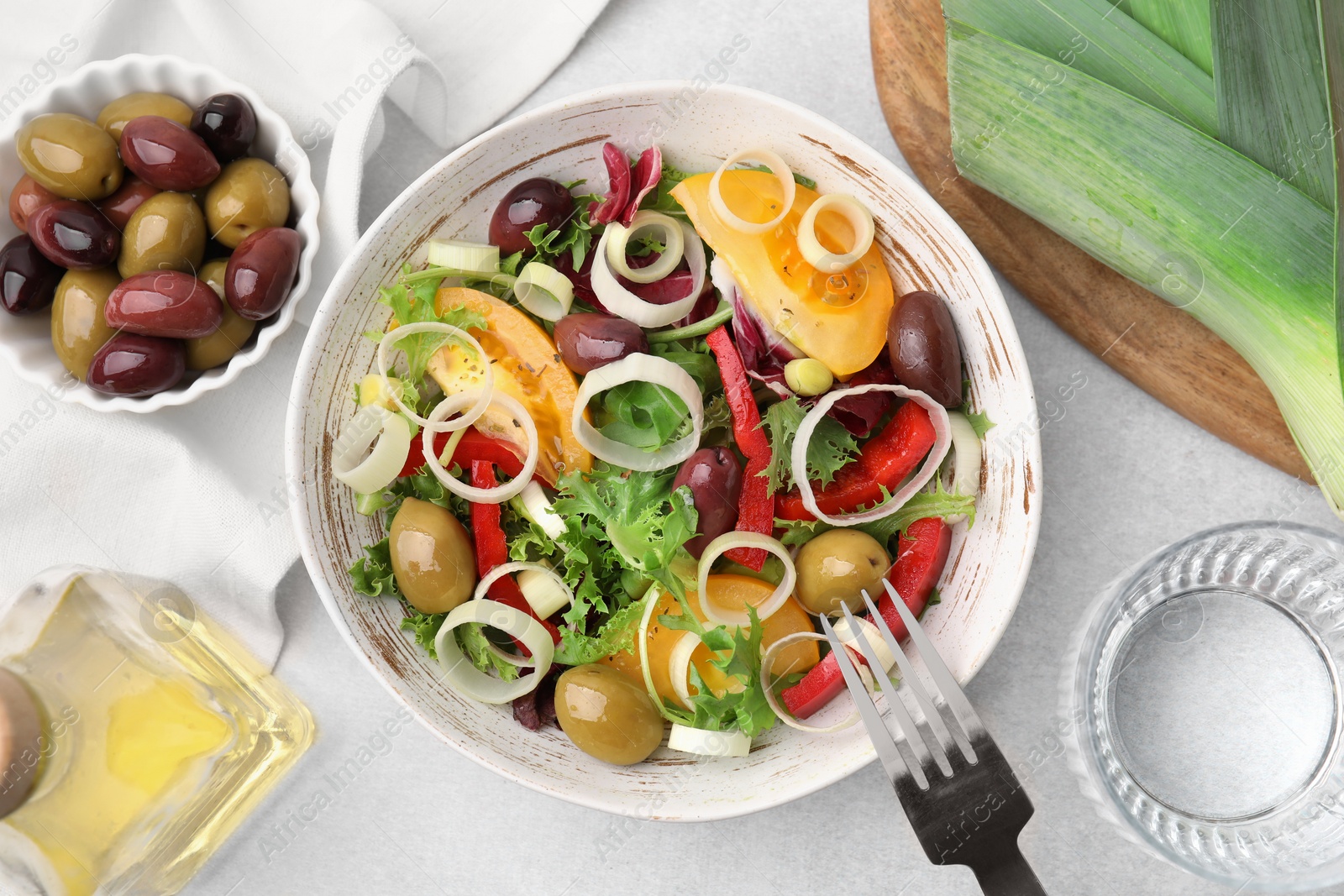 Photo of Bowl of tasty salad with leek and olives served on light table, flat lay