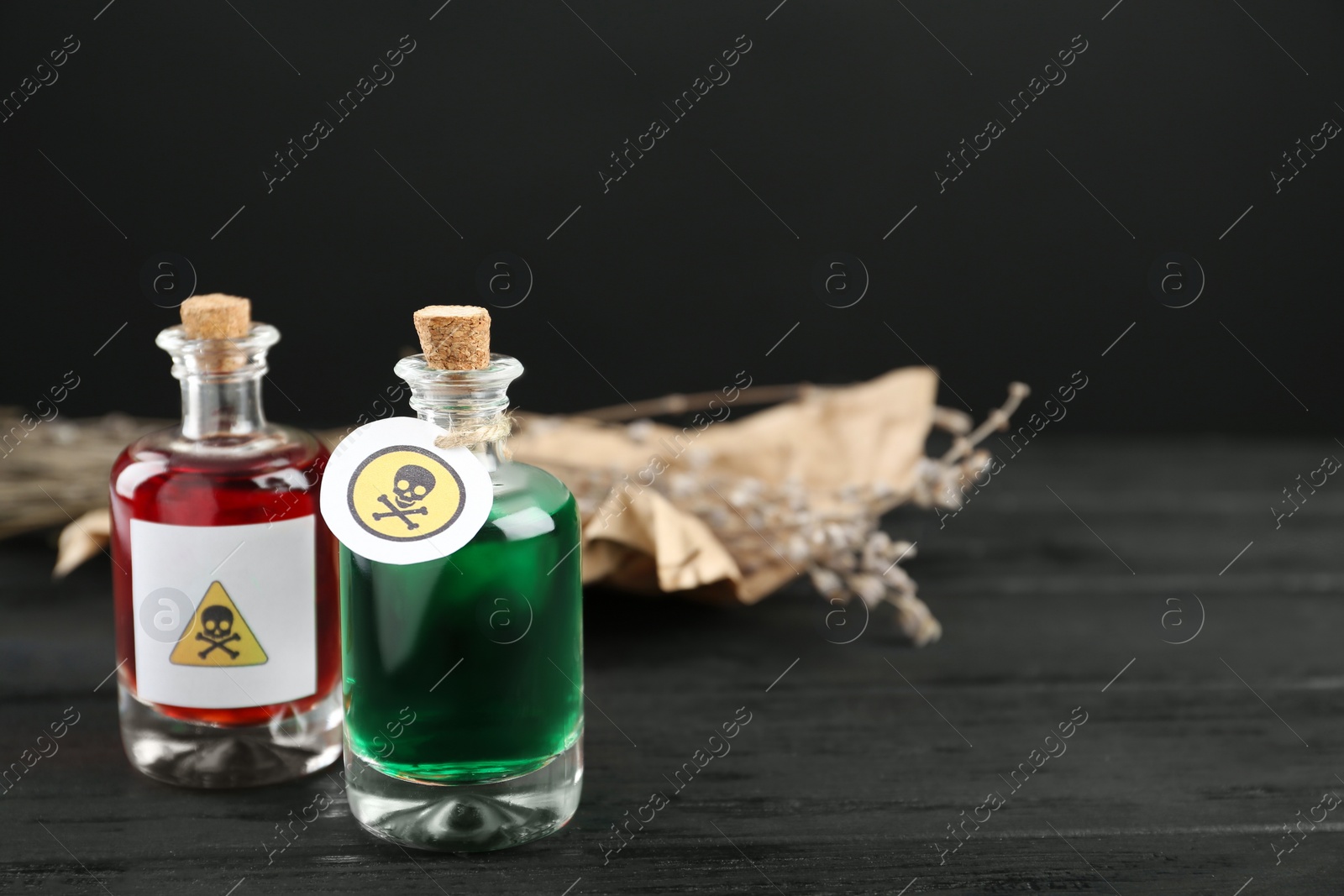 Photo of Glass bottles of poisons with warning signs on black wooden table. Space for text