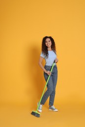 Photo of African American woman with green broom on orange background