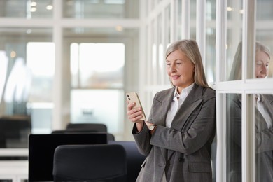Photo of Smiling woman with smartphone in office, space for text. Lawyer, businesswoman, accountant or manager