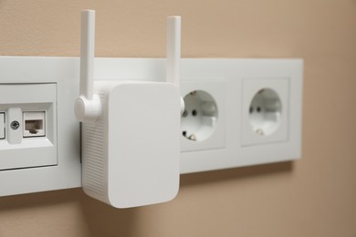 Wireless Wi-Fi repeater in power socket on beige wall, closeup