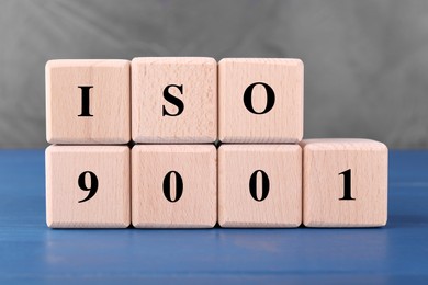 Photo of International Organization for Standardization. Cubes with abbreviation ISO and number 9001 on blue wooden table