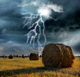 Image of Picturesque lightning storm over field with rolled hay bales