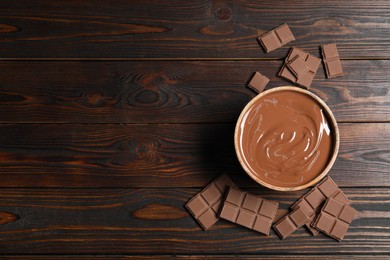 Tasty milk chocolate paste in bowl and pieces on wooden table, top view. Space for text