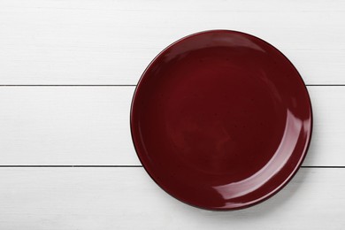 Photo of Empty burgundy ceramic plate on white wooden table, top view. Space for text