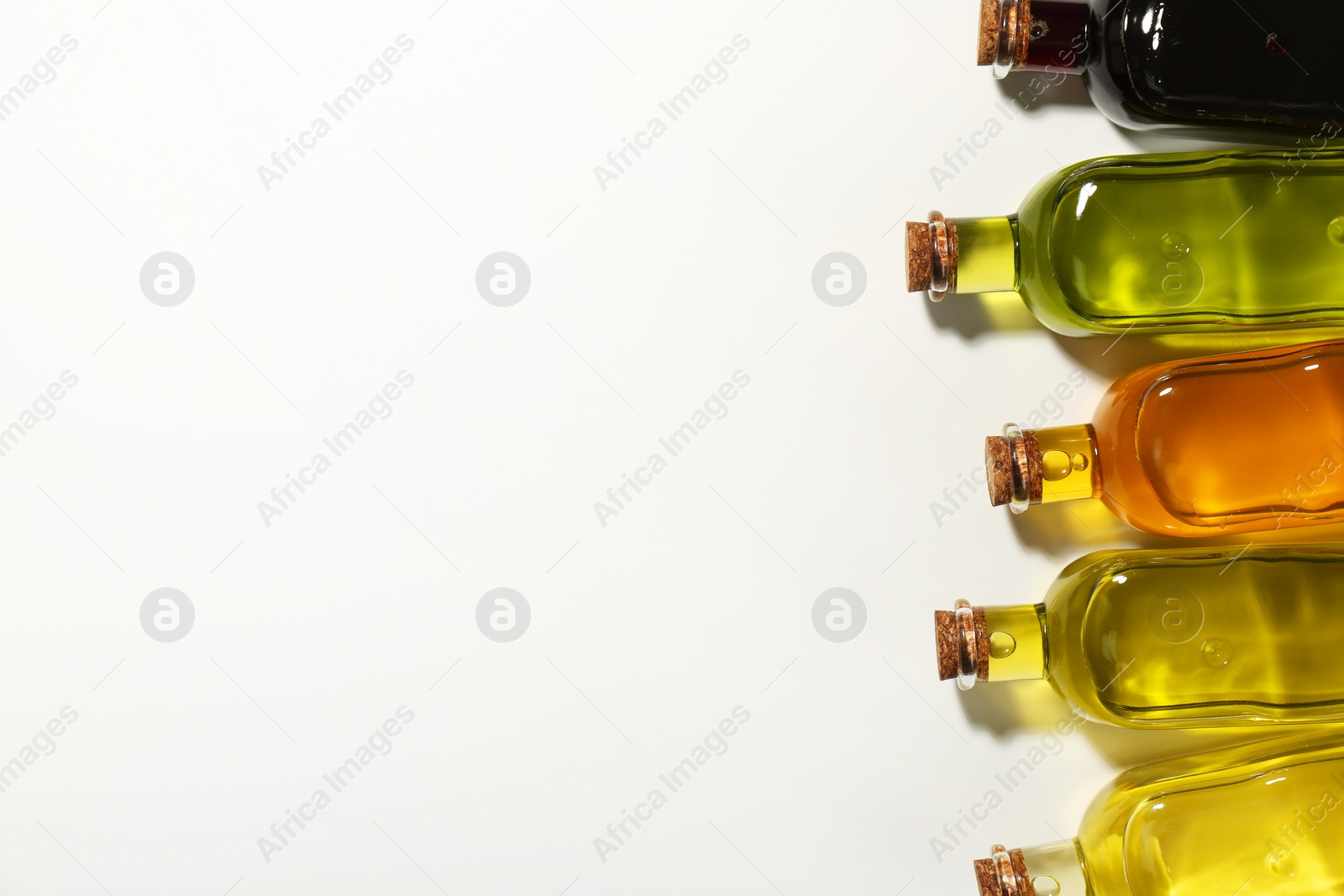 Photo of Vegetable fats. Different cooking oils in glass bottles on white background, flat lay. Space for text