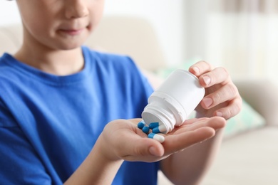 Photo of Little child with pills at home, closeup. Danger of medicament intoxication