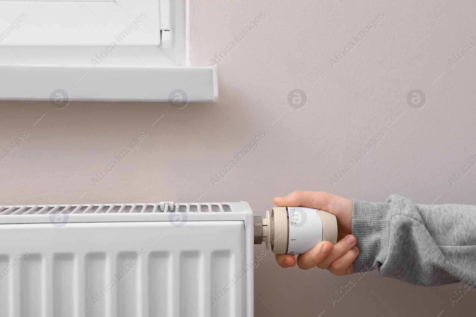 Photo of Girl adjusting heating radiator thermostat near white wall, closeup