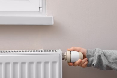 Photo of Girl adjusting heating radiator thermostat near white wall, closeup