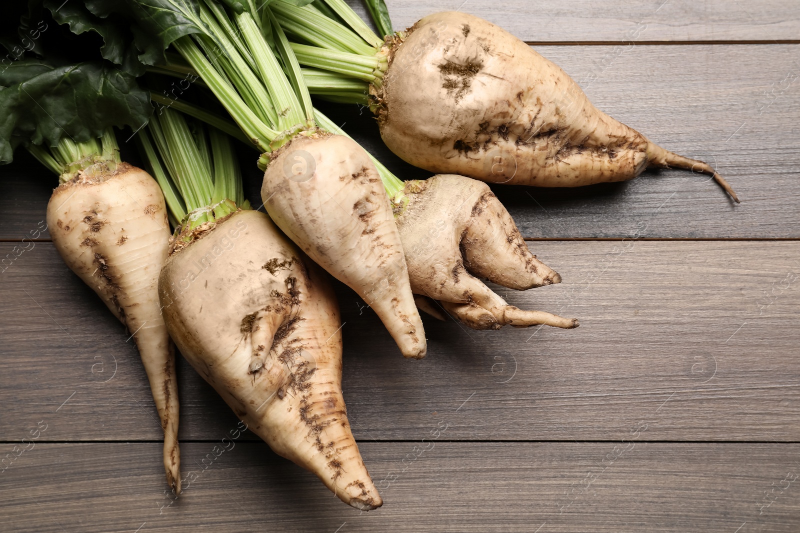 Photo of Fresh sugar beets with leaves on wooden table, flat lay