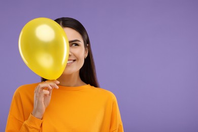 Photo of Happy woman with yellow balloon on purple background, space for text