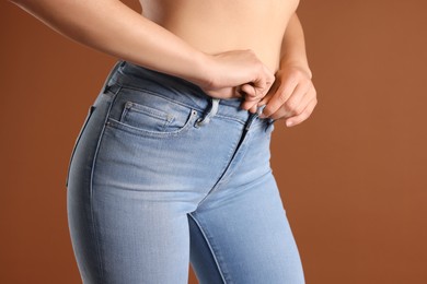 Photo of Woman wearing stylish light blue jeans on brown background, closeup
