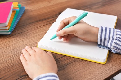 Woman writing in notebook at wooden table, closeup