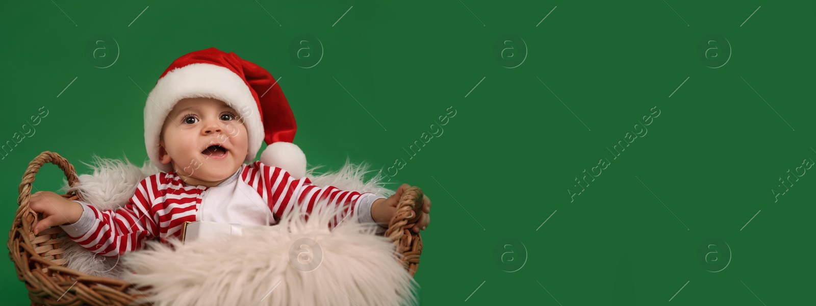 Image of Cute baby in wicker basket on green background, banner design with space for text. Christmas celebration