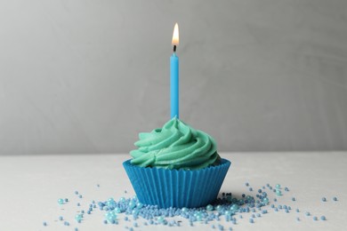 Delicious birthday cupcake with cream and burning candle on table