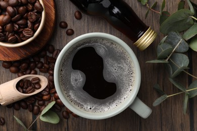 Cup of aromatic coffee, syrup, eucalyptus leaves and beans on wooden table, flat lay