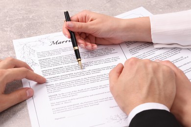 Photo of Man and woman signing marriage contract at light grey table, closeup