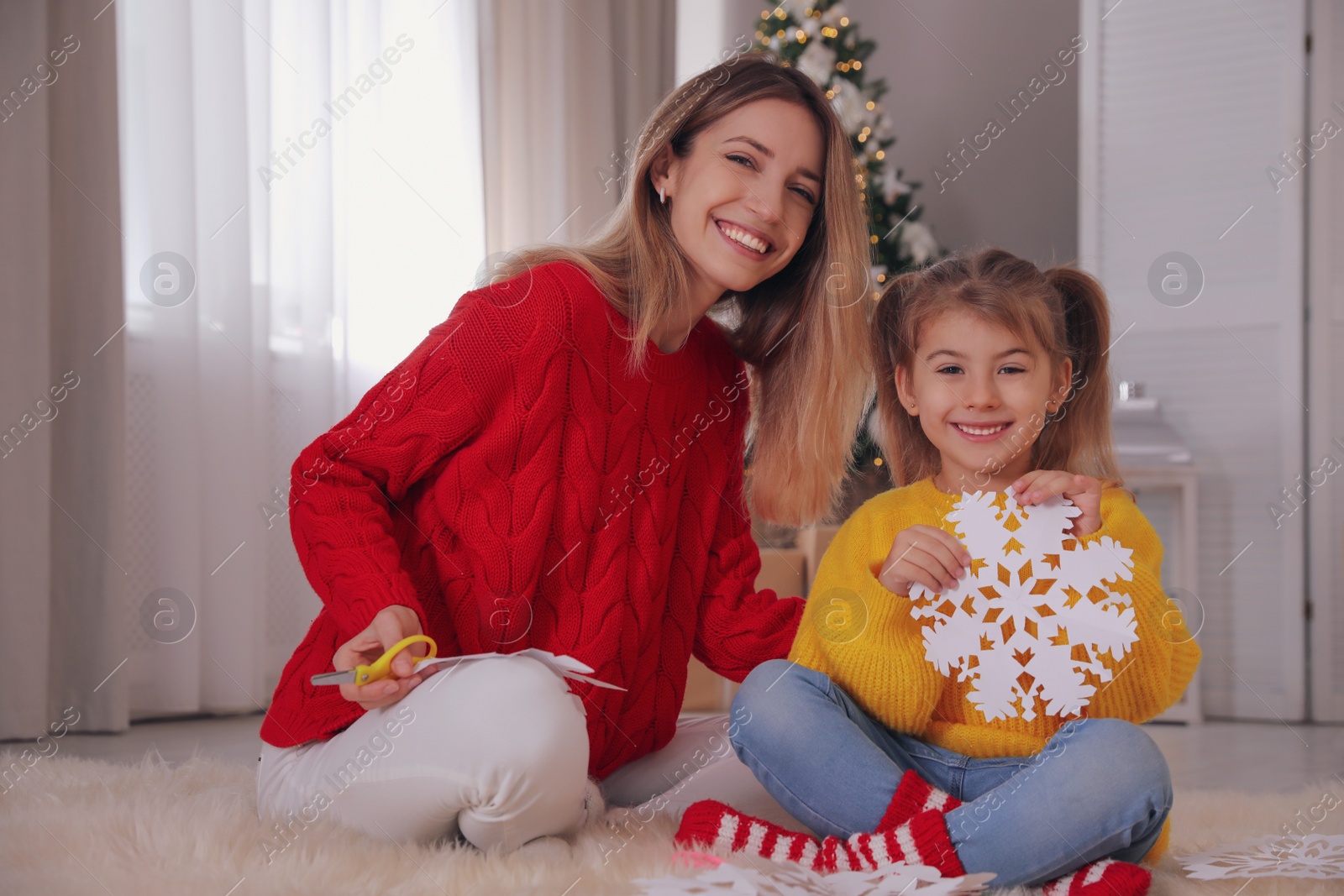 Photo of Happy mother and daughter with paper snowflake near Christmas tree at home