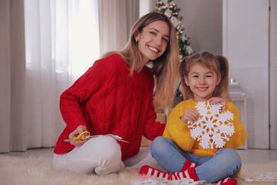 Photo of Happy mother and daughter with paper snowflake near Christmas tree at home