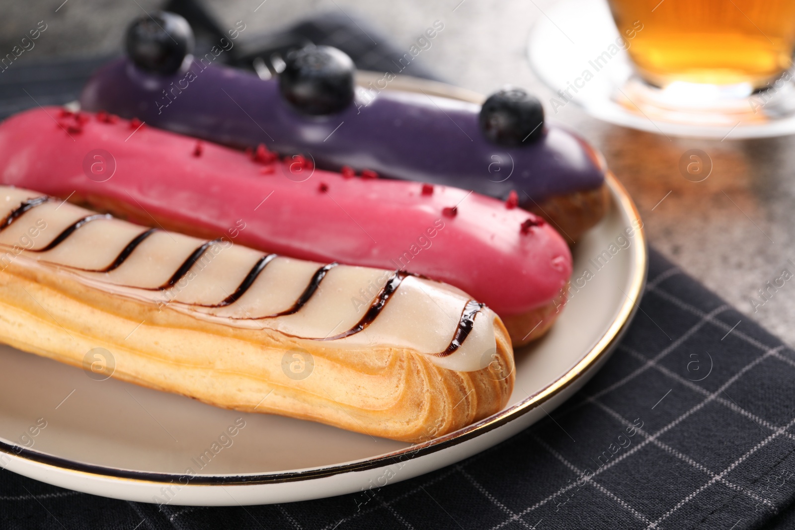 Photo of Plate with different tasty glazed eclairs on table, closeup