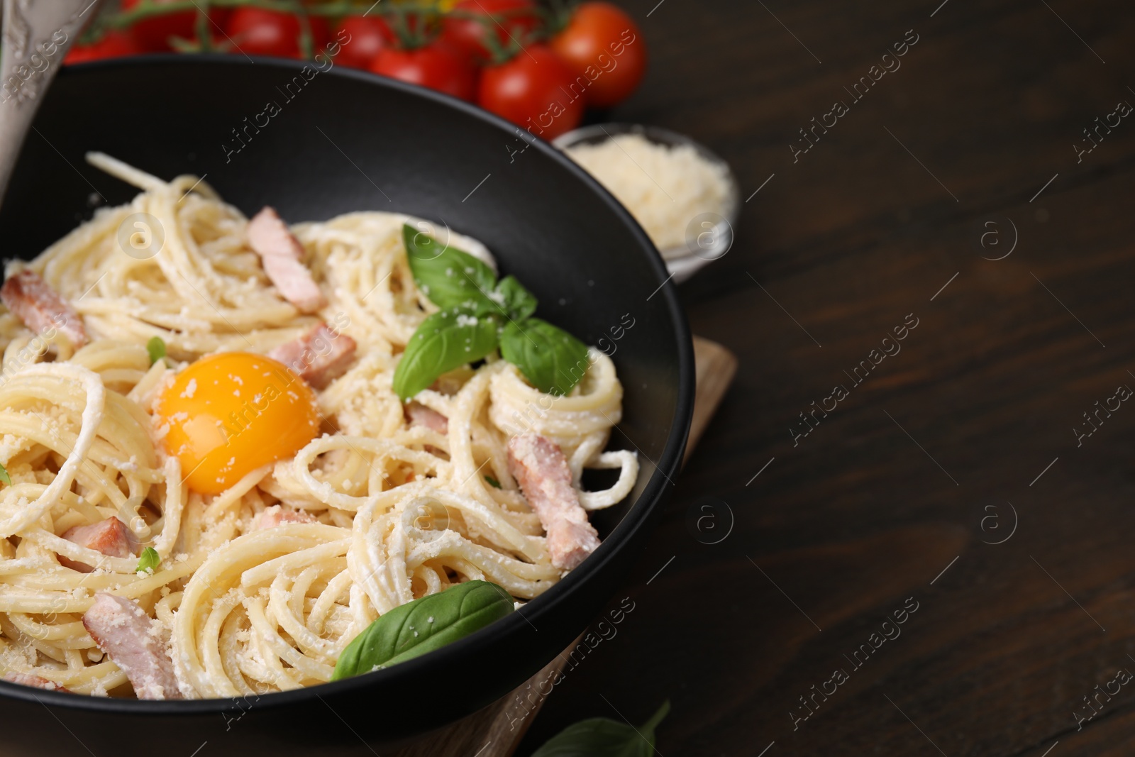 Photo of Bowl of delicious pasta Carbonara with egg yolk on wooden table, closeup. Space for text